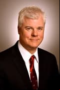 Commissioner Daniel McCarthy wearing black blazer and red striped tie.